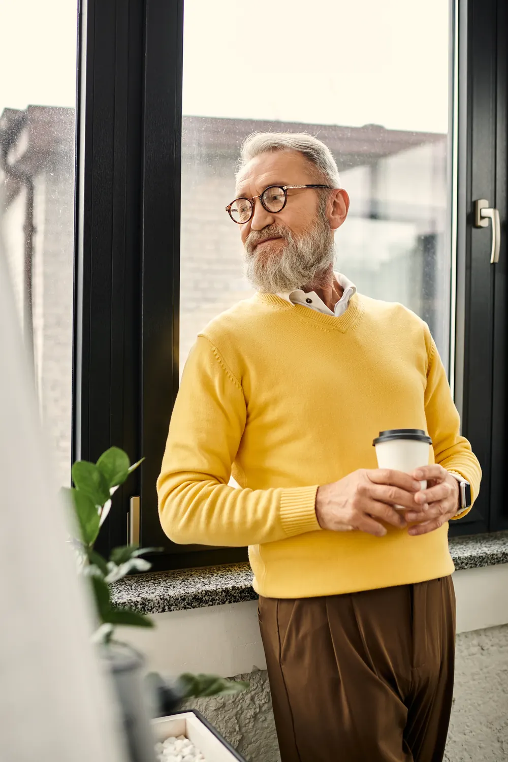 Pessoa tomando café junto à janela de casa, olhando para fora com calma